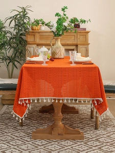 Detail of orange hollow crochet lace tablecloth with white cotton tassels on wood table