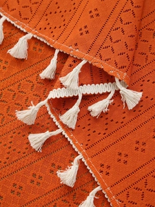 Close-up of orange hollow lace tablecloth with cream fringe tassels and crochet texture