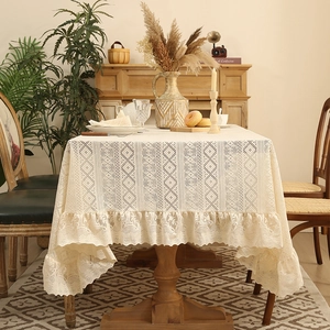 Vintage beige lace tablecloth with ruffle edges and geometric patterns on a wooden dining table