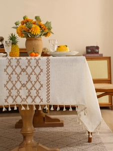 Close-up of linen tablecloth featuring brown geometric embroidery and elegant beige tassels