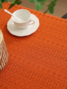 Detailed view of orange knitted hollow lace tablecloth with delicate crochet floral pattern