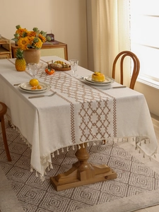 Detail of beige linen tablecloth featuring brown geometric embroidery and elegant fringe tassels