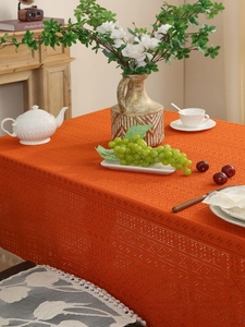 Close-up of bright orange crochet lace tablecloth with geometric patterns and white tassels