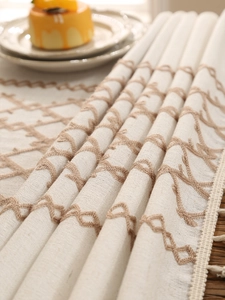 Close-up of linen tablecloth with geometric diamond embroidery and tassel detail