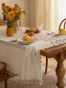 Detail of off-white linen table runner featuring brown geometric embroidery and fringe