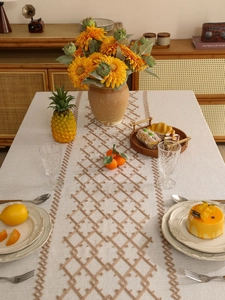 Detail of cream linen table runner featuring brown geometric diamond embroidery and scalloped edges