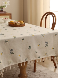 Detailed embroidery of floral patterns on linen tablecloth with beige tassel fringe edge
