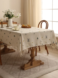 Detail of linen tablecloth featuring floral embroidery and elegant cream fringe tassels