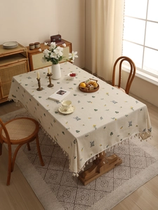Close-up of beige linen tablecloth featuring delicate floral embroidery and fringed edges