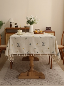 Detail of floral embroidery and white tassels on a cream-colored linen tablecloth