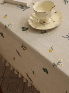 Detailed close-up of pastoral floral embroidery and fringe on beige linen tablecloth