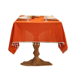 Hollow lace orange tablecloth with white fringe tassels on a vintage wood table