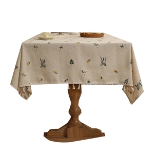 Linen embroidered tablecloth with floral patterns and white pompom tassel edges on a table