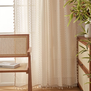 Detailed shot of beige lace curtain with hollow floral patterns and bohemian tassels