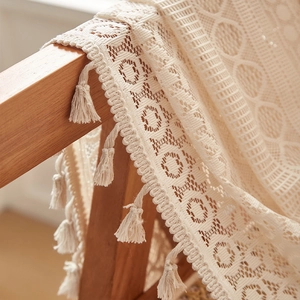 Detail of cream lace crochet blanket featuring geometric hollow patterns and handmade tassels