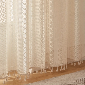 Detail of retro ivory lace curtain featuring geometric patterns and bohemian tassel fringe
