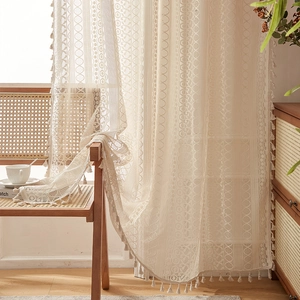 Detail of vintage beige lace curtain with geometric crochet patterns and tassel fringe