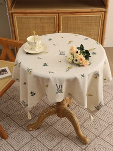 Close-up of beige linen round tablecloth featuring floral embroidery and tassel fringe edges