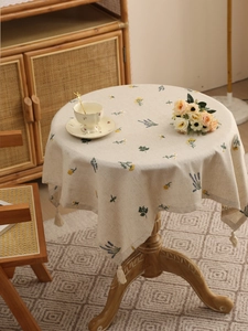 Detailed close-up of beige linen round tablecloth with floral embroidery and tassel edge