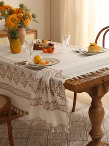 Close-up of beige linen tablecloth with brown floral embroidery and fringe details