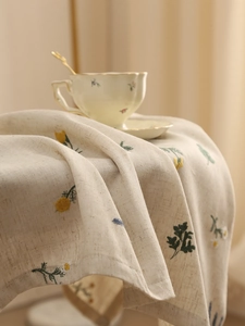 Detail of floral embroidery on beige linen tablecloth with daisy and leaf patterns