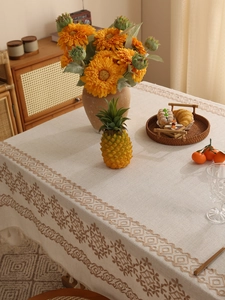 Detailed close-up of linen tablecloth featuring brown geometric embroidery and fringe edges