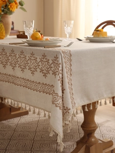 Close-up of linen tablecloth featuring brown geometric embroidery and elegant tassel edges
