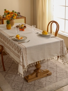 Detail of beige linen tablecloth with dark brown embroidery and delicate tassel edges