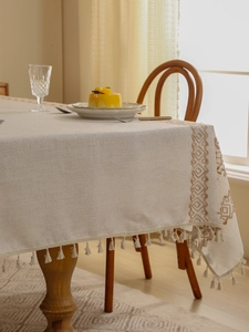 Detail of beige linen tablecloth featuring geometric embroidery and fringe tassels