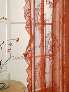 Vista detallada de la cortina de encaje naranja con motivos florales y bordes con volantes