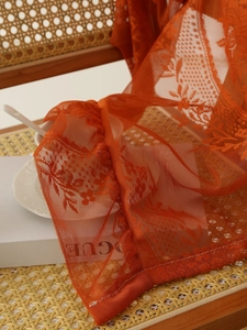 Detalle de tela de encaje naranja caramelo con bordado floral en una silla tejida