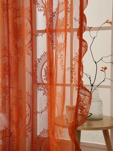 Detalle de cortina de encaje naranja con bordado floral y elegante borde festoneado