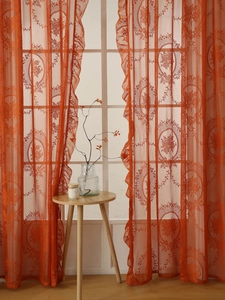 Detalle de cortina de encaje naranja con motivos florales y borde con volantes