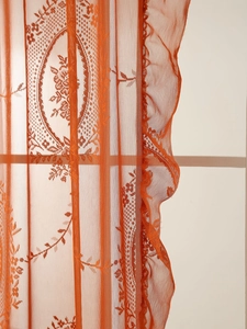 Detalle de cortina de encaje naranja vintage con bordado floral y bordes con volantes