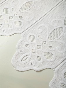 Detail of white lace cafe curtain with delicate floral patterns and scalloped edges