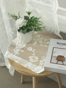 Detail of white lace tablecloth with vintage rose patterns on a wooden table