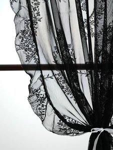 Detail of black French floral lace curtain with ribbon tie and mesh embroidery texture