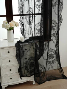 Detail showing vintage black lace curtain with floral embroidery and wavy edges on window