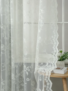 Close-up of white lace curtain with delicate floral patterns and scalloped edges