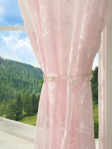 Detail of pink floral lace curtain with pearl tieback against a nature window view