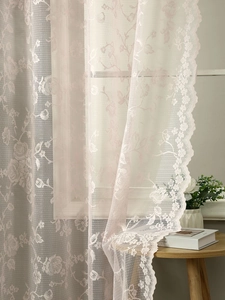 Close-up of light pink lace curtain with floral embroidery and scalloped edges