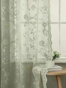 Close-up of light green French lace curtain with elegant rose patterns and wavy edges