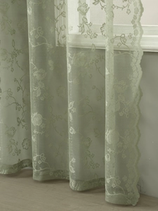 Detail view of light green lace curtain with elegant floral patterns and scalloped edges