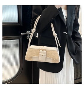 Detail showing white and beige faux crocodile skin texture and metal buckle on handbag