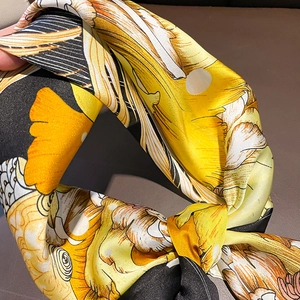 Close-up of smooth silk scarf fabric featuring yellow ginkgo leaf and floral art prints