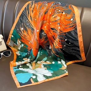 Detail of silk satin scarf featuring orange fish and green floral patterns on leather couch