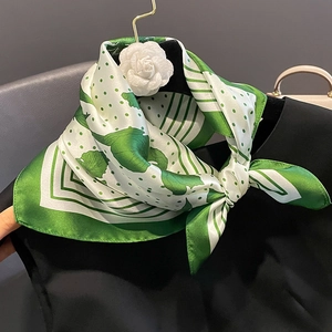 Elegant green and white silk square scarf with floral print tied on a black garment neck