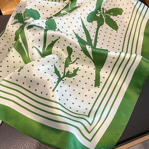 Close-up of silk square scarf featuring green polka dots and elegant floral patterns