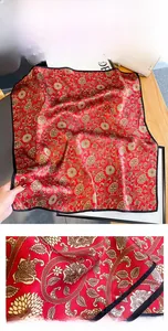 Detail of red silk scarf with golden floral patterns and black stitched edges
