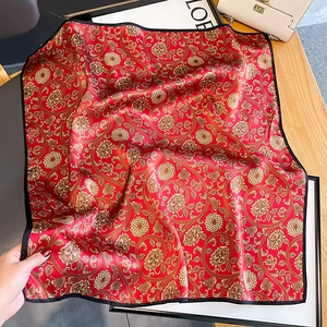 Elegant red silk scarf with golden floral patterns and black border laid on wooden table